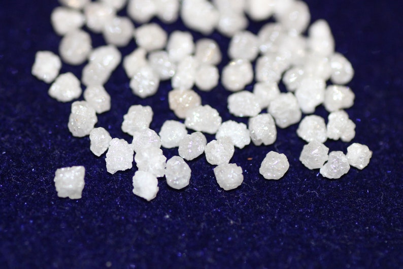 Op de afbeelding: Een close-up van een stapel kleine, witte, ruwe diamanten op een donkerblauw fluwelen oppervlak.