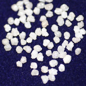 Op de afbeelding: Een close-up van een verzameling kleine, witte, ruwe diamanten die verspreid liggen op een donkerblauw oppervlak.