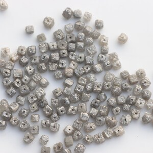 May include: A pile of small, gray, square-shaped diamonds. The diamonds are all about the same size and have a rough, unpolished texture.