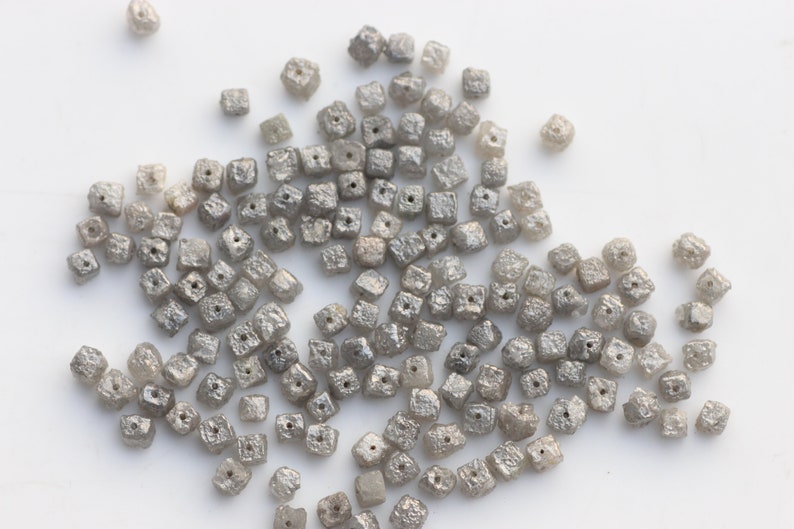 May include: A pile of small, gray, square-shaped diamonds. The diamonds are all about the same size and have a rough, unpolished texture.