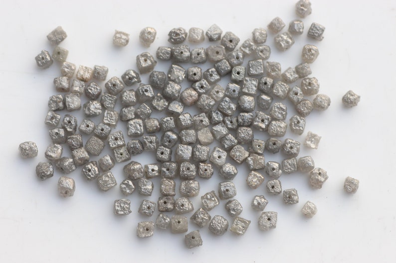 May include: A pile of small, gray, square-shaped diamonds. The diamonds are rough and have a matte finish.