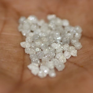 Op de afbeelding: Een hoop kleine, witte, ruwe diamanten op iemands hand.