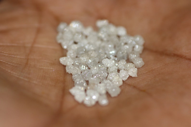 Op de afbeelding: Een hoop kleine, witte, ruwe diamanten op iemands hand.