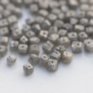 May include: A close-up of a pile of small, gray, square-shaped diamonds. The diamonds are rough and have a matte finish.
