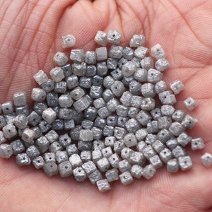 May include: A pile of small, gray, square-shaped diamonds. The diamonds are rough and have a matte finish.