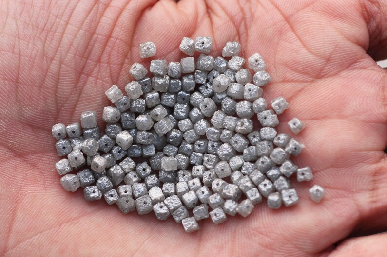 May include: A pile of small, gray, square-shaped diamonds. The diamonds are rough and have a matte finish.