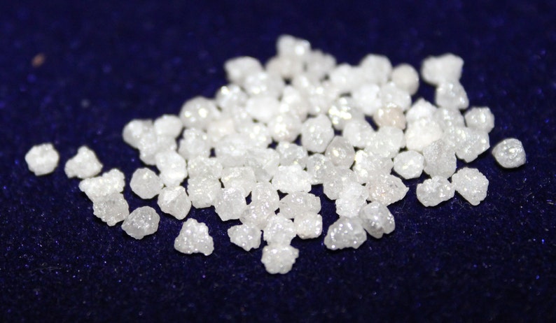 Op de afbeelding: Een hoop kleine, witte, ruwe diamanten op een donkerblauwe achtergrond.