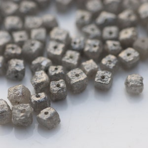 May include: A close-up of a pile of small, gray, square-shaped diamonds. The diamonds are rough and have a matte finish.