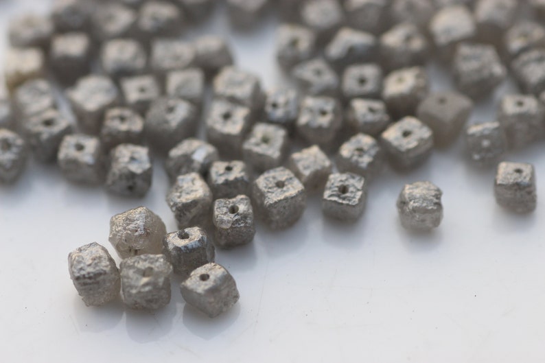 May include: A close-up of a pile of small, gray, square-shaped diamonds. The diamonds are rough and have a matte finish.