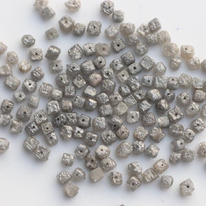 May include: A pile of small, gray, square-shaped diamonds. The diamonds are rough and have a matte finish.