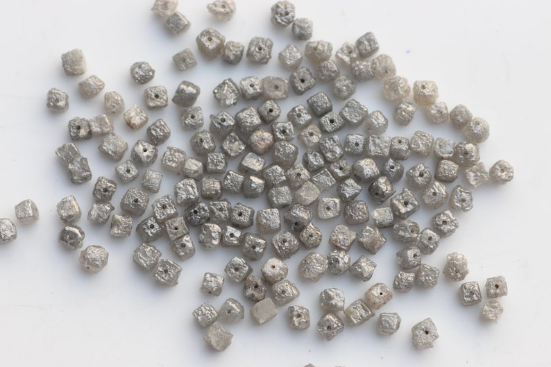 May include: A pile of small, gray, square-shaped diamonds. The diamonds are rough and have a matte finish.