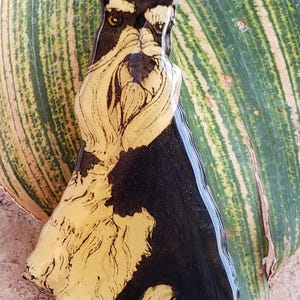 May include: A glossy, decorative figurine of a dog, primarily black and tan, with a detailed depiction of the dog's features. The figurine is set against a backdrop of green and yellow striped leaves, creating a striking contrast.