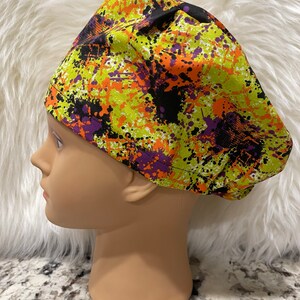 May include: A green, orange, purple, and black patterned scrub hat with a splatter paint design.