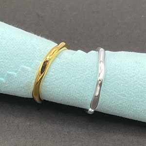 May include: Two simple, thin, metal rings. One ring is gold and the other is silver. The rings are on a light blue cloth.