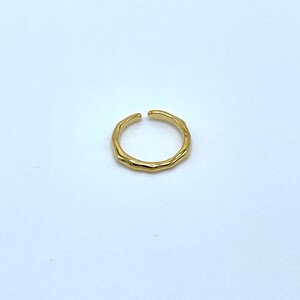 May include: A gold-toned, textured, open ring. The ring is made of metal and has a simple, minimalist design.