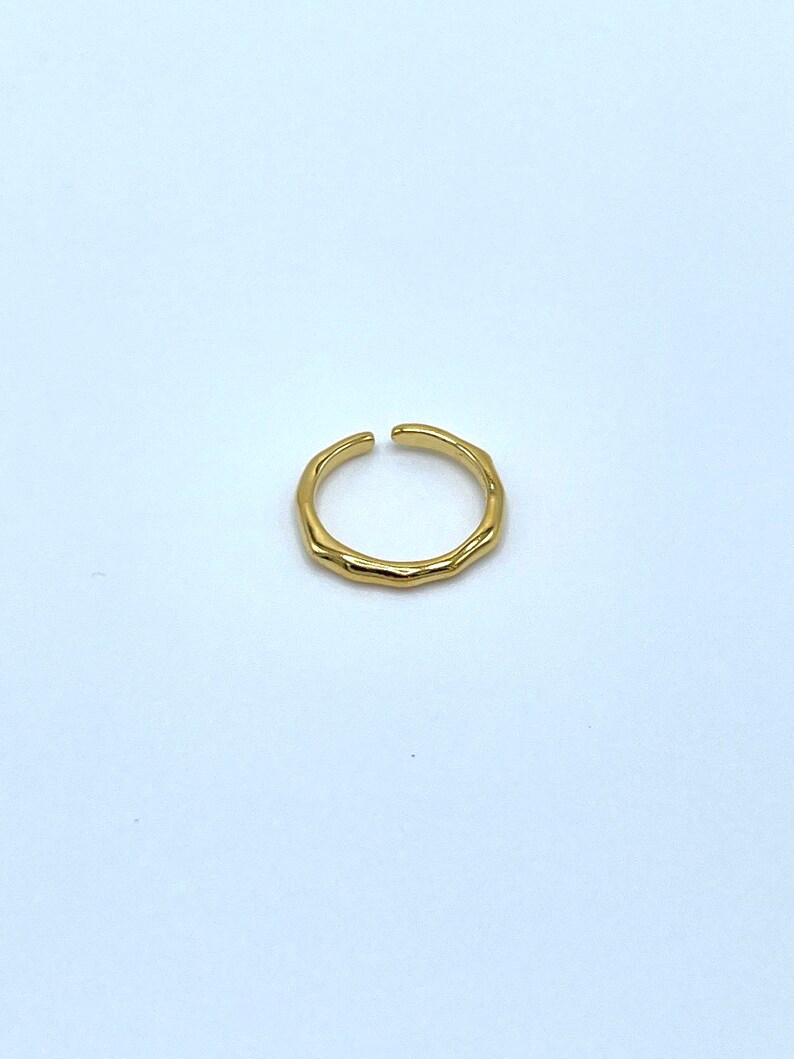 May include: A gold-toned, textured, open ring. The ring is made of metal and has a simple, minimalist design.
