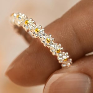 May include: A silver ring with a band of small daisy flowers with gold centers.