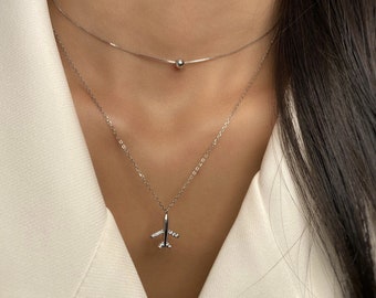 May include: A silver necklace with a small airplane pendant and a silver chain with a small ball pendant.