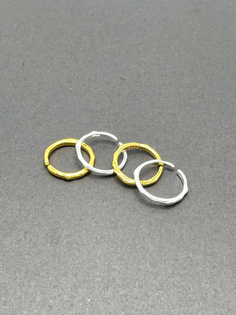 May include: Four silver and gold rings, stacked on a grey surface. The rings are all different sizes and have a textured finish.