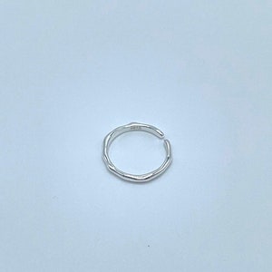 May include: A silver ring with a textured, irregular band. The ring is open and has a slight gap on one side.
