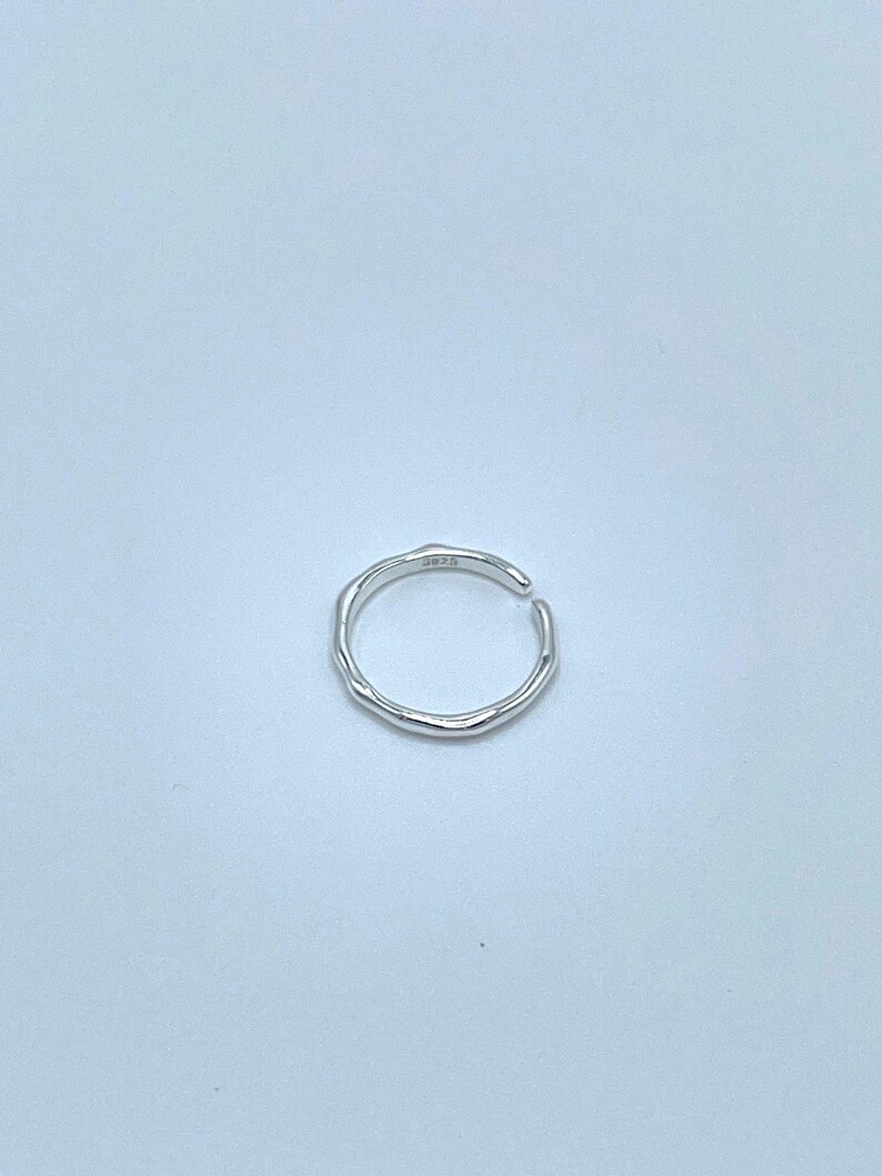 May include: A silver ring with a textured, irregular band. The ring is open and has a slight gap on one side.