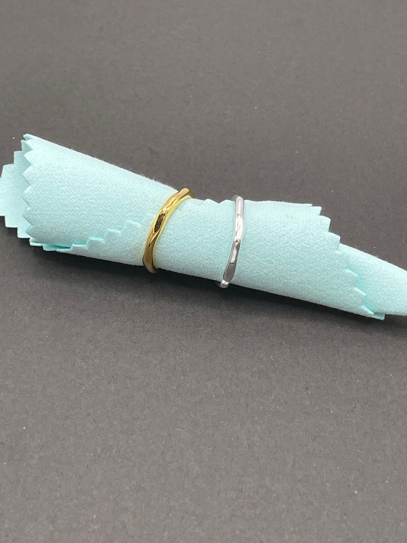 May include: Two simple, thin, metal rings. One ring is gold and the other is silver. The rings are on a light blue cloth.