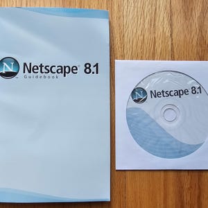 May include: A light blue Netscape 8.1 guidebook with a circular logo and the text Netscape 8.1 Guidebook, alongside a white paper sleeve containing a compact disc featuring the same Netscape 8.1 logo and text printed on the disc surface.