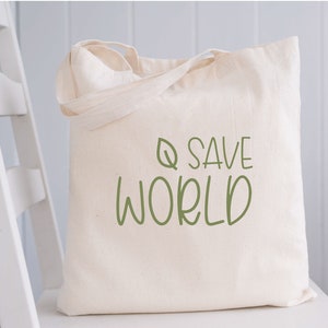 Pode incluir: Uma bolsa tote de lona branca com texto verde que diz "Q SAVE WORLD" e um pequeno desenho de folha verde.