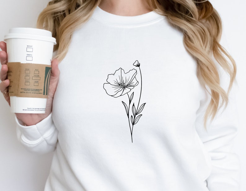 Puede incluir: Sudadera blanca con un dibujo de l&iacute;nea negra de una flor en la parte delantera.