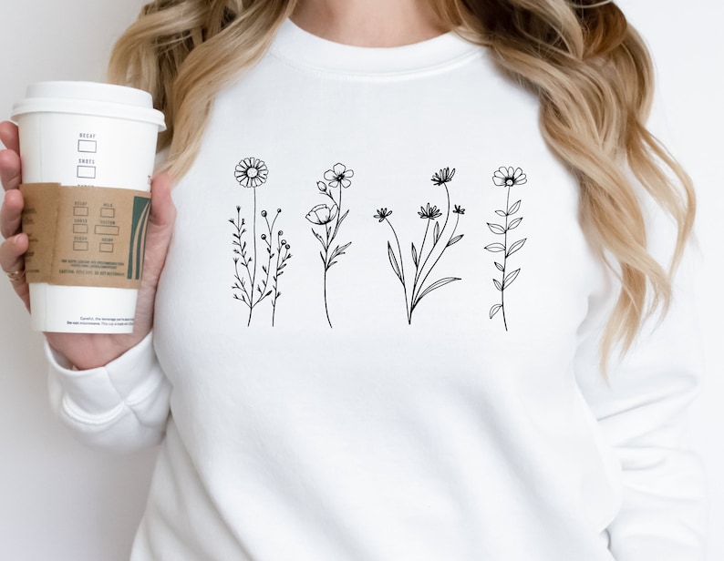 Puede incluir: Sudadera blanca con un dibujo de l&iacute;nea negra de cinco flores y tallos diferentes.