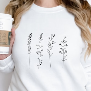 Puede incluir: Sudadera blanca con un dibujo de l&iacute;nea negra de cinco tipos diferentes de flores silvestres.