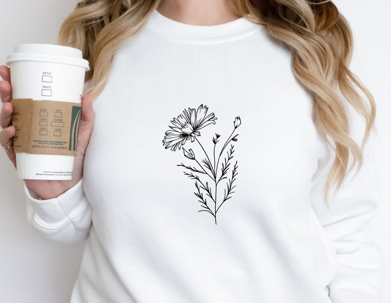 Puede incluir: Una sudadera blanca con un dibujo de l&iacute;nea negra de una flor en la parte delantera.