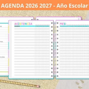 Puede incluir: Una colorida agenda escolar para 2026-2027, con secciones para asistencia y planificación mensual. El cuaderno abierto muestra páginas rayadas, con encuadernación en espiral. Incluye un lápiz arcoíris y un lápiz dorado. El texto "AGENDA 2026 2027 - Año Escolar" está en la parte superior.