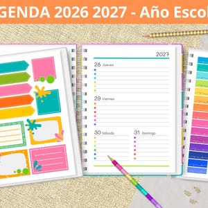 Könnte beinhalten: Spiralgebundenes Notizbuch mit farbenfrohen, stickerartigen Seiten. Das Notizbuch trägt die Aufschrift "AGENDA 2026 2027 - Año Escolar" und enthält Daten für 2027. Die Seiten zeigen verschiedene Formen und Farben, darunter Rosa, Grün, Orange und Blau.