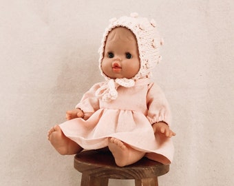 May include: A pink doll wearing a pink dress and a white crocheted hat sits on a wooden stool.