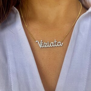 以下が含まれることがあります： ダイヤモンドがちりばめられたペンダントが「Viriato」という名前を綴る、金のチェーンネックレスです。