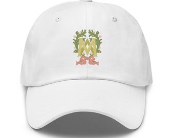 May include: White baseball cap with a decorative emblem. The emblem features a gold letter "M" surrounded by green leaves, pink accents, and a pink ribbon. The cap is made of a soft fabric and has a curved brim.