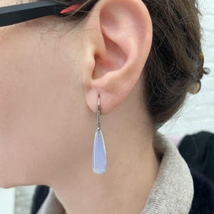 May include: A pair of silver teardrop earrings with a light purple gemstone and a row of small clear stones on the dangle.