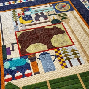 Peut inclure: Une courtepointe colorée avec un ours brun, une théière bleue, un poisson vert et une boussole. La courtepointe est faite de différents tissus et a un design matelassé.