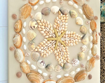 May include: A beige canvas with a circular design made of seashells. The center of the design features a gold starfish surrounded by smaller seashells. The outer ring of the design is made of larger seashells in shades of brown and white.