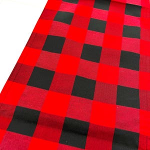 May include: A red and black buffalo check table runner. The runner features a classic plaid pattern with alternating red and black squares. The fabric appears to be a woven material, suitable for a dining table or other decorative purposes.