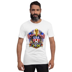 May include: White t-shirt featuring a colorful graphic design for the FIFA World Cup 2026. The design includes the USA flag, a soccer ball, a trophy, and the text "USA" and "FIFA WORLD CUP 2026".