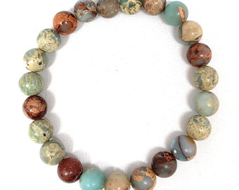 May include: A bracelet made of round, multi-colored stones. The stones are a mix of brown, green, and beige.