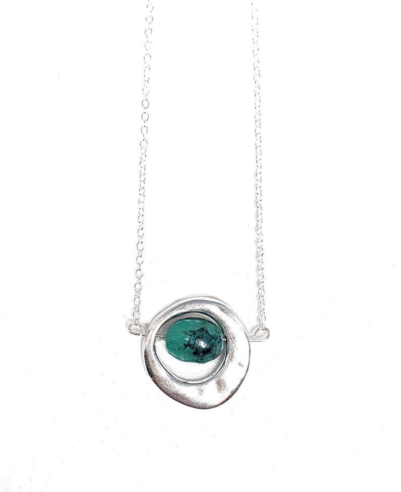 May include: A silver necklace with a circular pendant featuring a green gemstone. The pendant is made of two overlapping circles, with the gemstone nestled in the center.