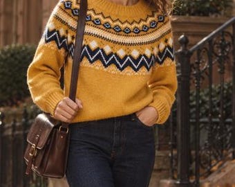 May include: A mustard yellow long-sleeve sweater featuring a dark navy blue and white geometric Fair Isle pattern across the chest and shoulders, paired with dark blue denim jeans and a brown leather crossbody bag with a gold-tone buckle.