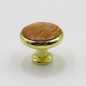 May include: A round, gold-colored cabinet knob with a woodgrain top. The knob has a smooth, shiny finish.