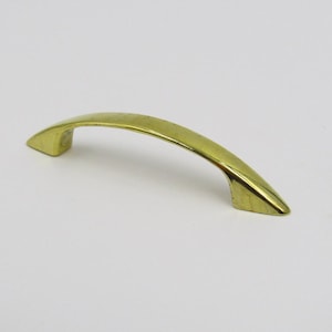 May include: A gold-toned metal cabinet pull with a curved shape.