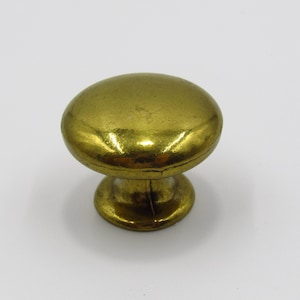 Peut inclure: Un bouton de porte en métal doré avec un dessus rond et une base légèrement surélevée.