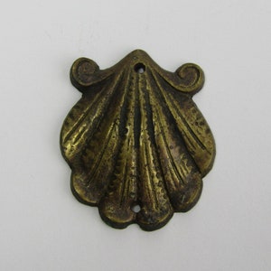Op de afbeelding: Een gouden metalen schelp ornament met een gedetailleerd ontwerp. Het ornament heeft een gat aan de bovenkant om op te hangen.