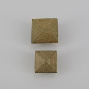 May include: Two wooden pyramid-shaped blocks. The top block is larger than the bottom block.